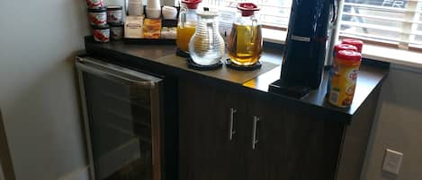 A kitchen counter with a refrigerator, a coffee maker, and various food items.