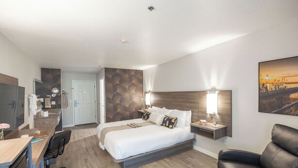 Ein Hotelzimmer mit Bett, Schreibtisch, Stuhl, Sofa, Fernseher und einem Bild an der Wand.