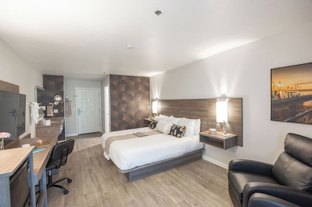 A hotel room with a bed, a desk, a chair, a sofa, a TV, and a painting on the wall.