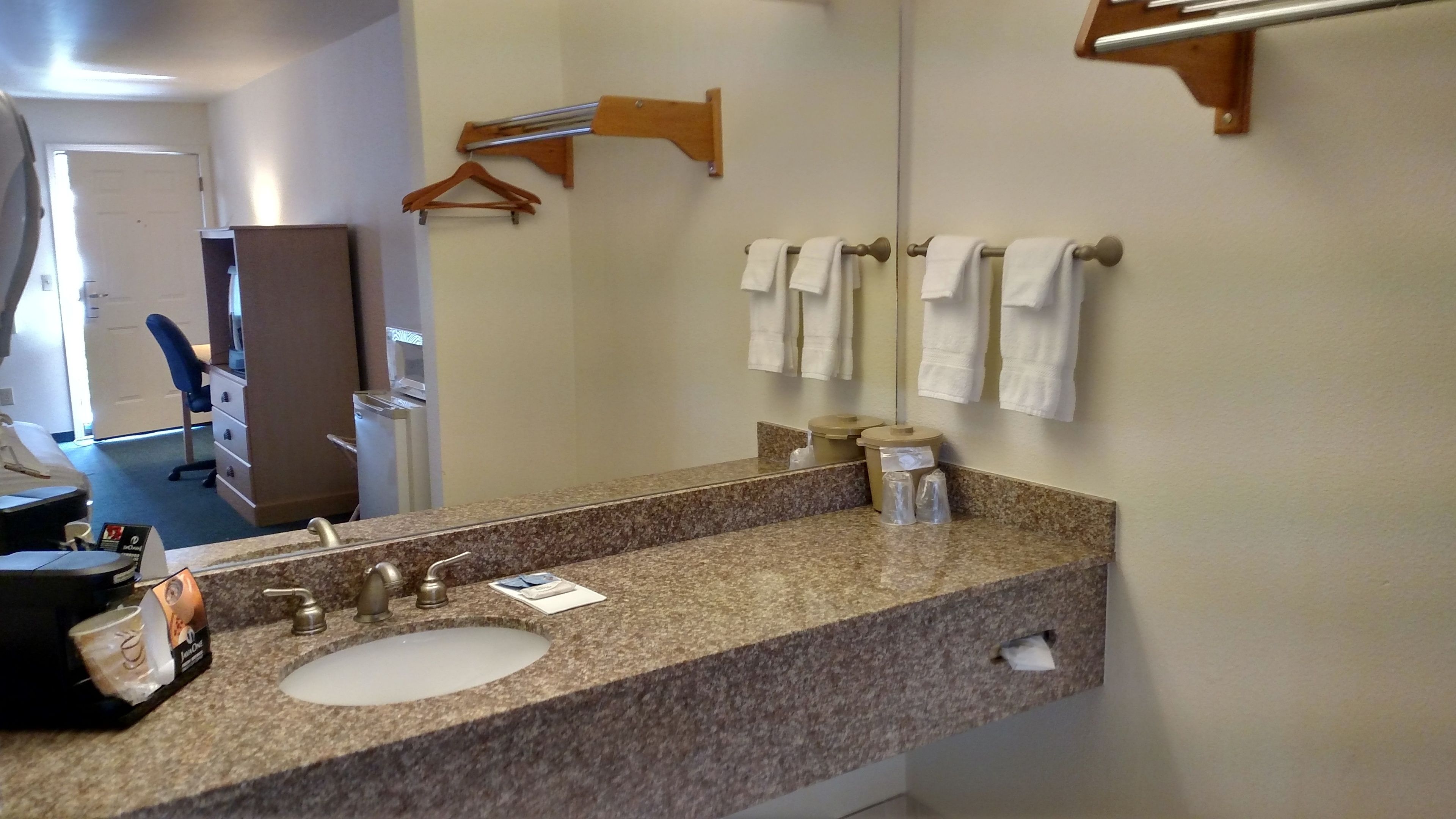 A bathroom with a granite countertop sink, a mirror, and a towel rack.