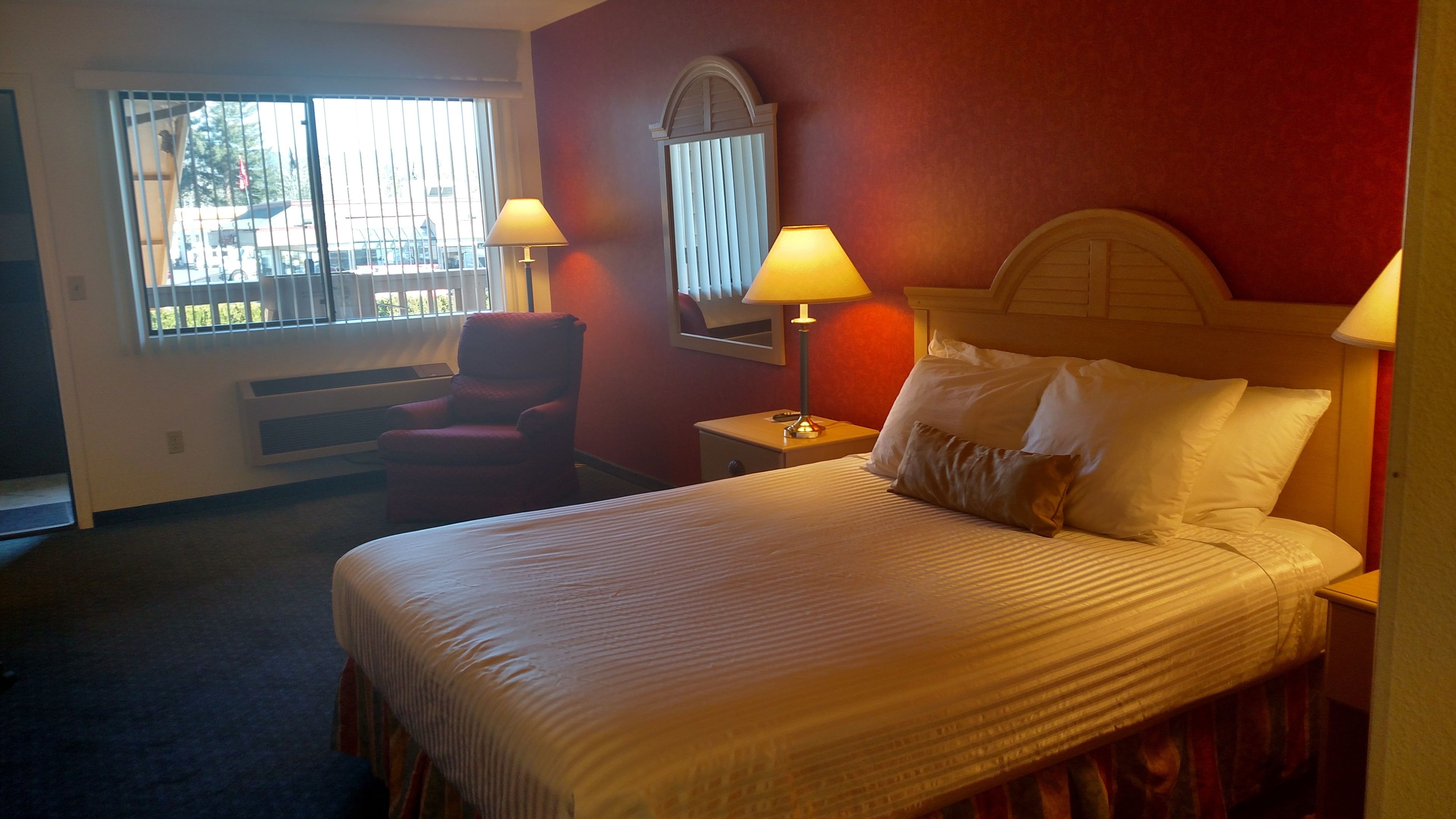 Een hotelkamer met een bed, twee bedlampen, een stoel, een raam met zonwering en een radiator.