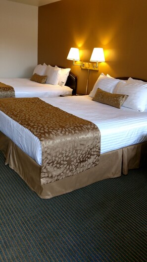 A hotel room with two beds, a large bedspread, two bedside lamps, and a carpeted floor.
