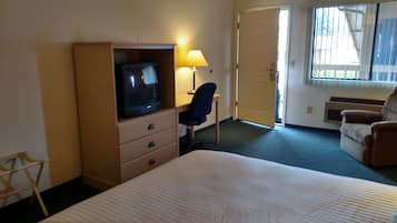 A hotel room with a bed, a desk with a chair, a television, and a window with blinds.
