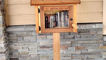 Una estantería de madera con un letrero que dice 'LittleFreeLibrary' frente a una pared beige con detalles de piedra.