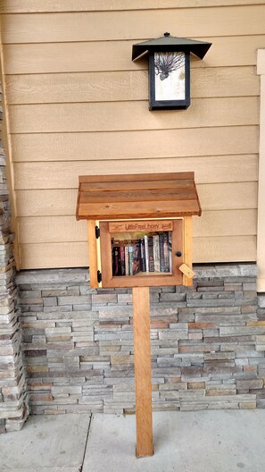 A wooden bookcase with a sign reading "LittleFreeLibrary" against a beige wall with stone accents. - Lewis River Inn (Woodland)