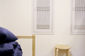 Een kamer met een bed, een kruk en twee ramen met tralies.