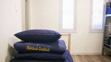 A single bed with blue bedding and a pillow labeled "Seoul Dalbit" in a room with white walls and a window.