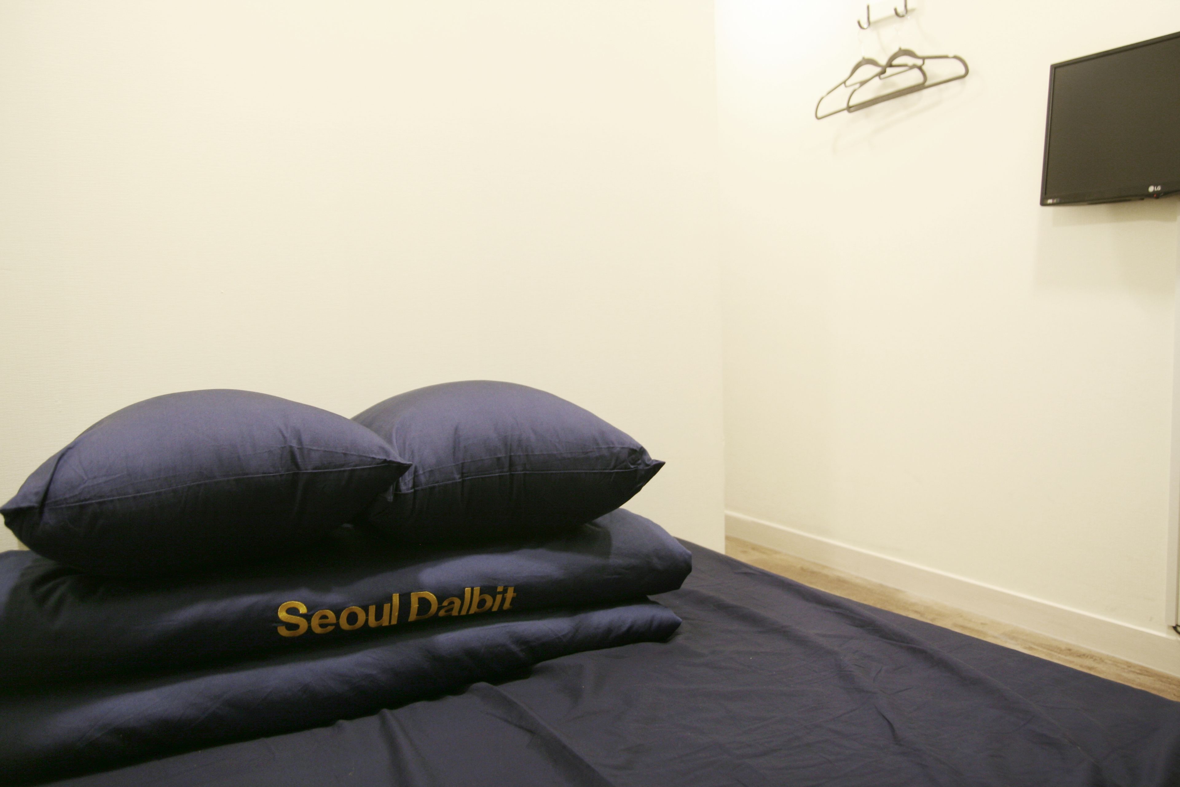 A bed with dark blue bedding and two pillows, one with "Seoul Dalbit" embroidered on it.
