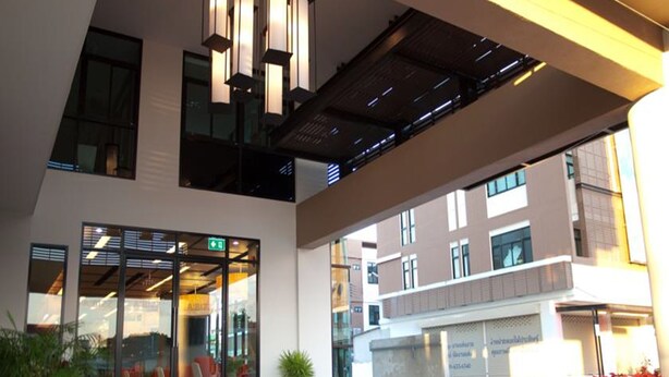 A modern building with large windows, a glass entrance, and a ceiling with exposed beams. - A Bizz (Lampang)