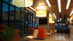 A modern lobby with glass walls, orange seating, and a polished floor. - A Bizz (Lampang)