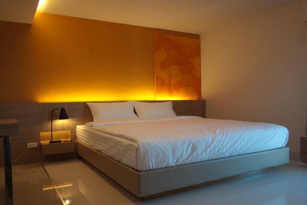 A modern bedroom with a large bed, a nightstand with a lamp, and a wall-mounted artwork.