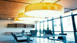 A modern meeting room with a glass table, black chairs, and yellow pendant lights. - A Bizz (Lampang)