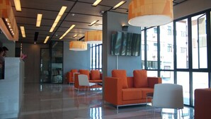 A modern lobby with orange seating, a flat-screen TV, and large windows. - A Bizz (Lampang)