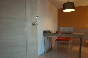 A modern room with a wooden door, a desk with a laptop, a chair, and a hanging light fixture.
