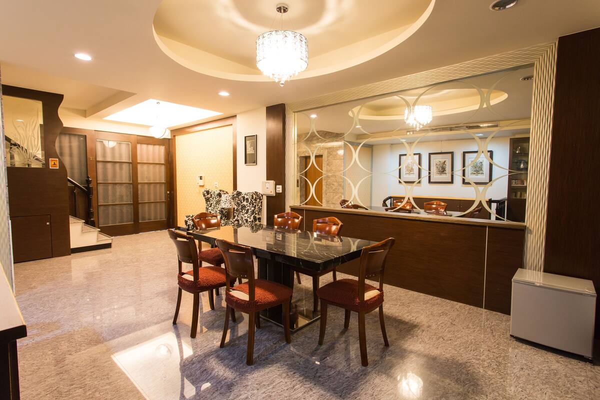 Uma área de refeições moderna, com piso de mármore, mesa com tampo de vidro e seis cadeiras de madeira com assentos acolchoados.