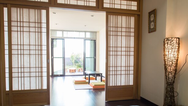 A traditional Japanese room with tatami flooring, a low table, and sliding doors leading to an outdoor area.