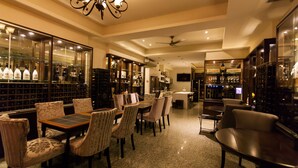 A spacious bar area with a long counter, multiple seating options including a bar stool and cushioned chairs, and a large wine display.