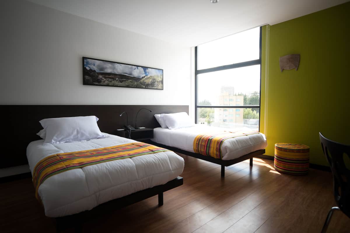 A hotel room with two beds, a large window, and a painting on the wall.
