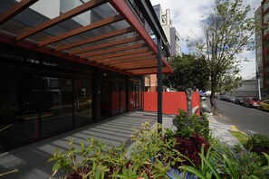 A modern building with a glass facade, a red awning, and a paved walkway with potted plants.