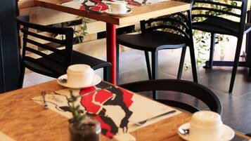 A café with wooden tables, black chairs, and red and white floral tablecloths.