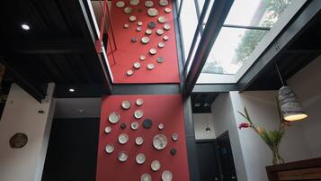 Un intérieur moderne avec un plafond haut, de grandes fenêtres et un mur rouge orné de motifs circulaires.