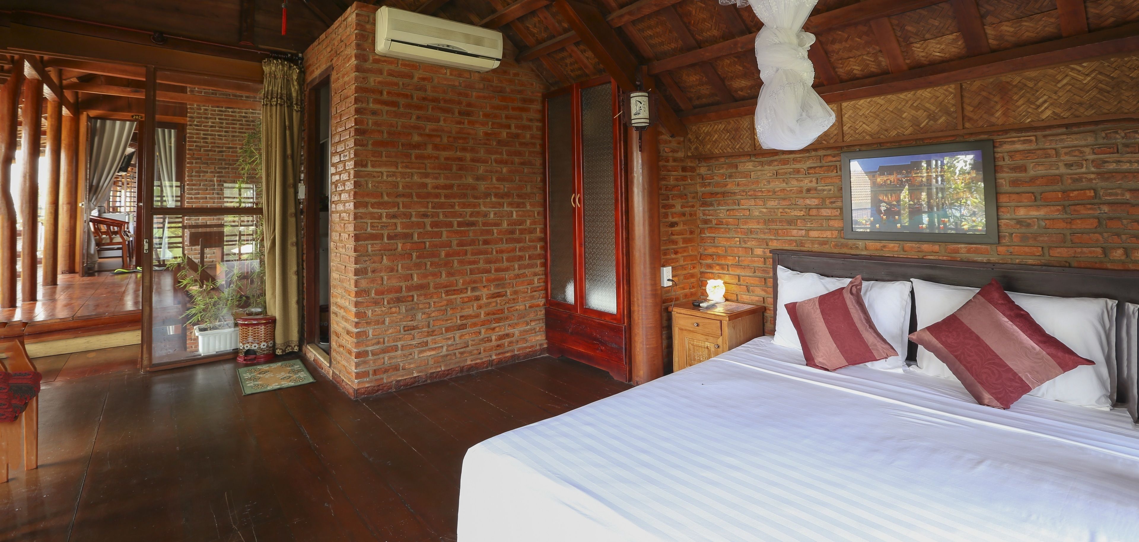 Ein Zimmer mit einem großen Bett, Holzboden, einer Ziegelwand und einem Deckenventilator.