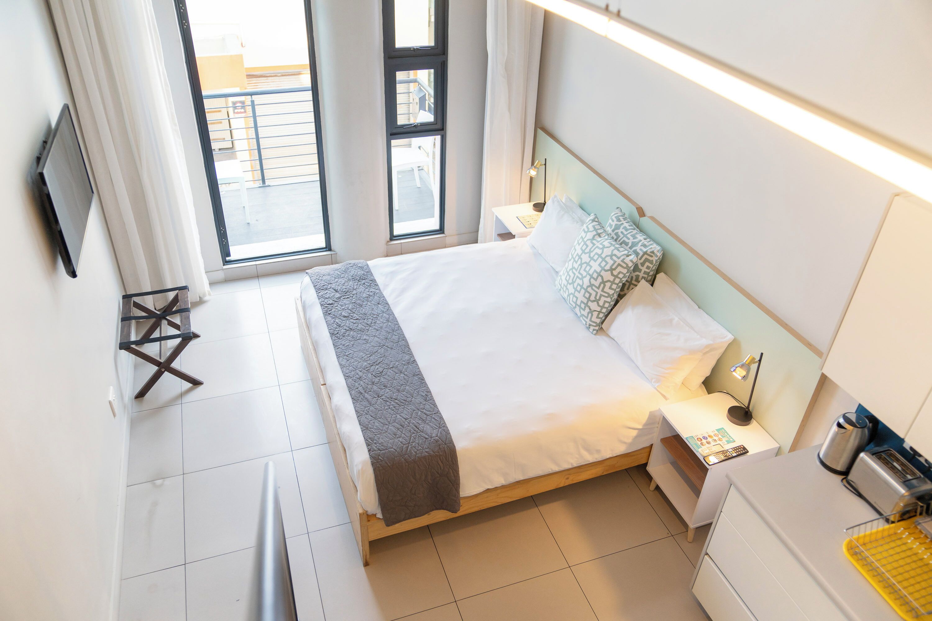 A hotel room with a bed, bedside table, lamp, and a flat-screen TV mounted on the wall.