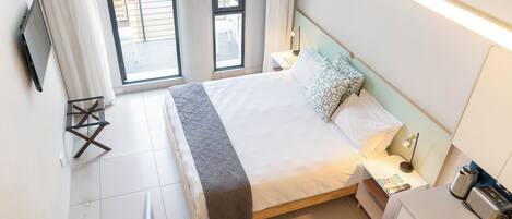 A hotel room with a bed, bedside table, lamp, and a flat-screen TV mounted on the wall.