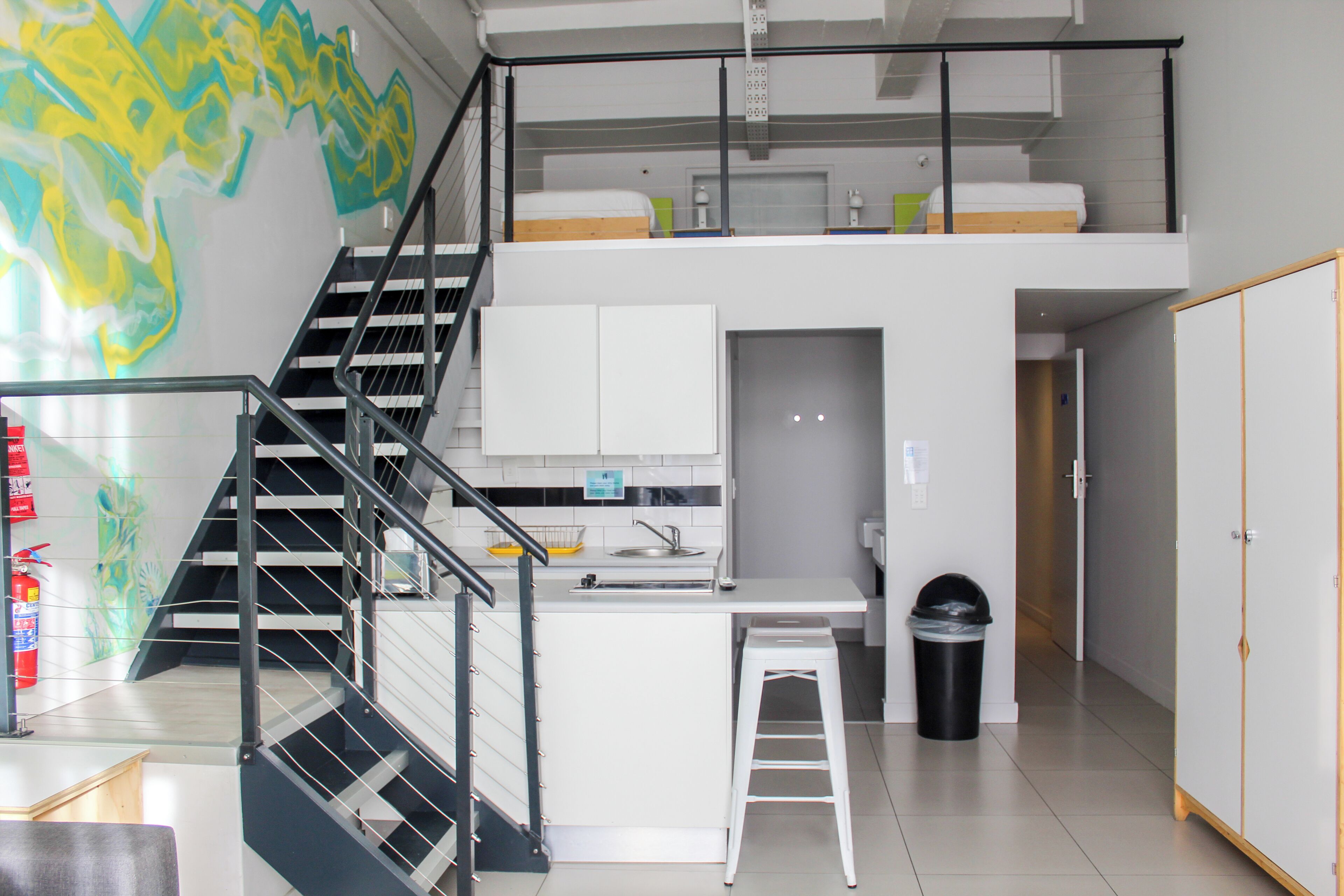 A modern apartment with a kitchen, a dining area, a staircase, and a loft bedroom.