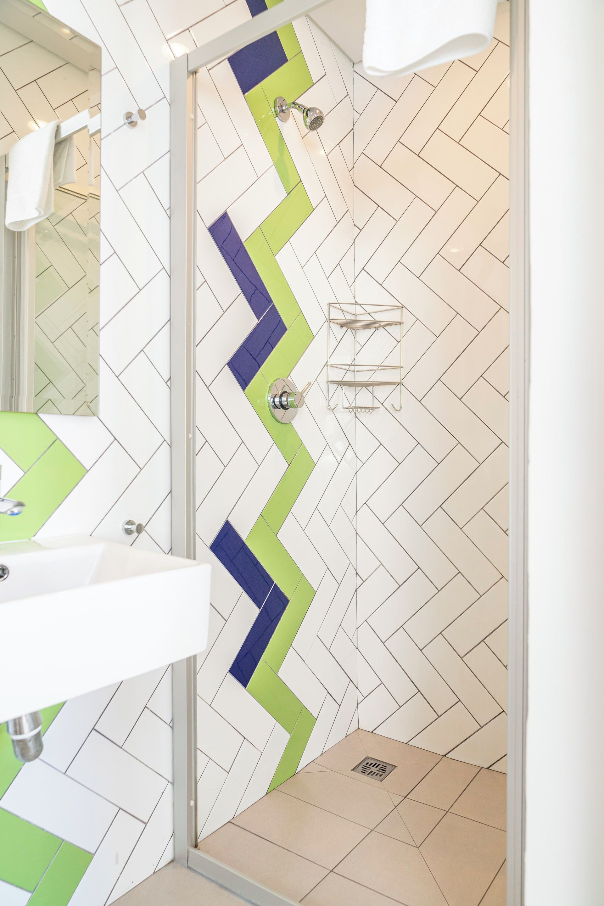A bathroom with a herringbone tile pattern, a glass shower enclosure, and a white sink.