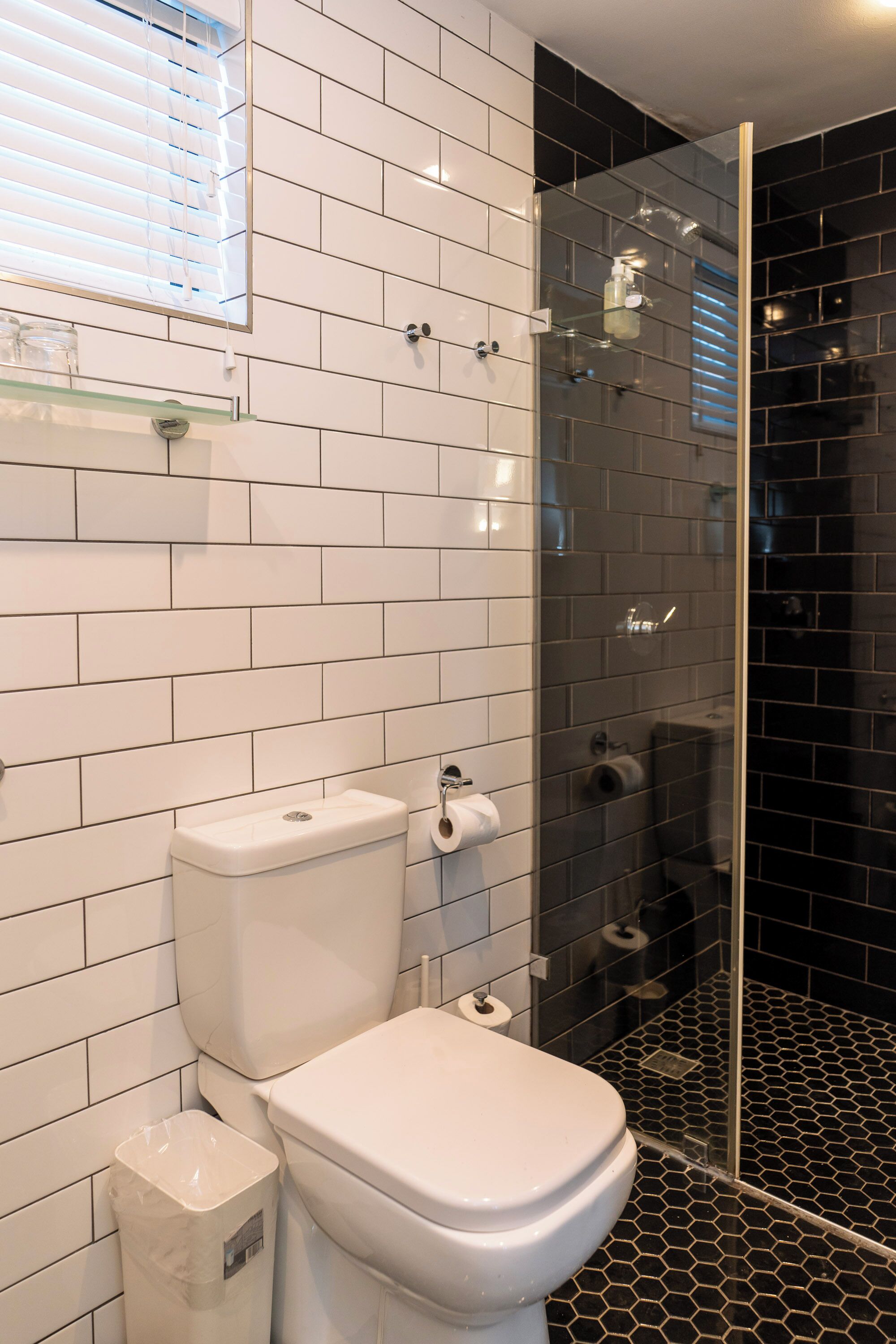 A bathroom with a white toilet, a glass shower enclosure, and a black tiled floor.