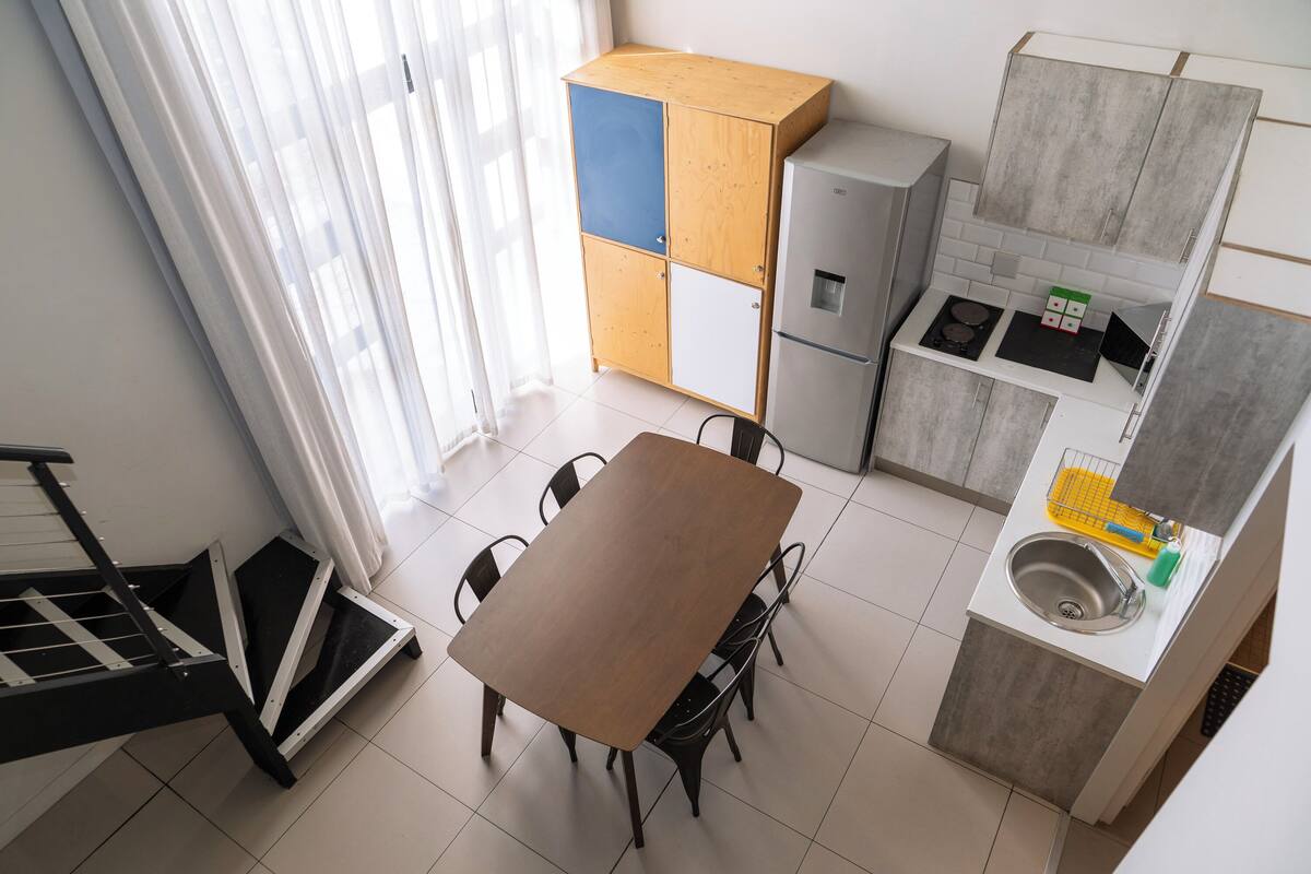 A compact kitchen with a dining table, chairs, a refrigerator, and a sink.