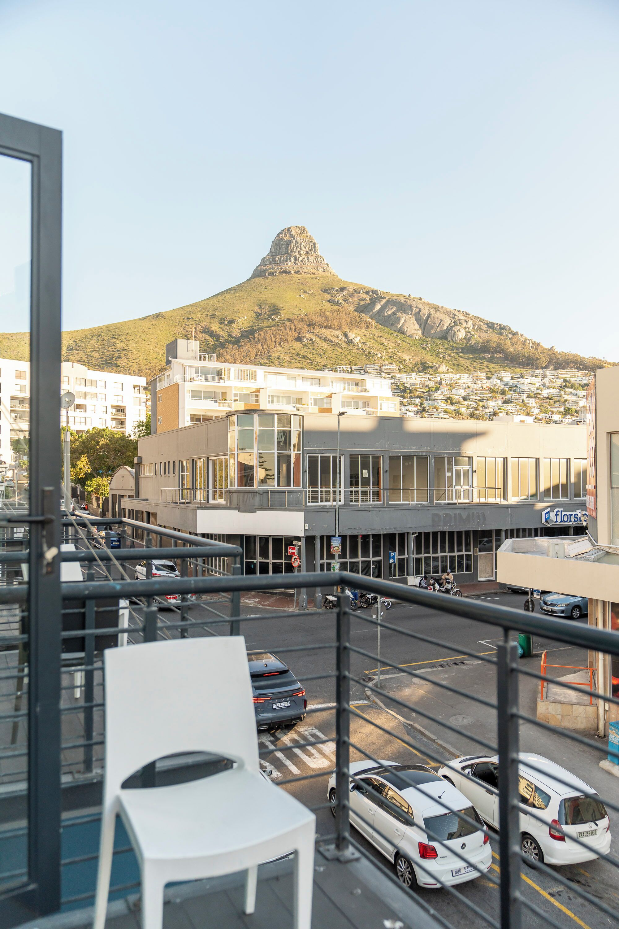 A balcony with a white chair, a view of a cityscape, and a mountain in the background.