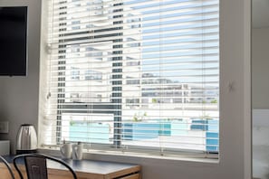 A room with a large window, a flat-screen TV mounted on the wall, a kettle, and a small table with two mugs.