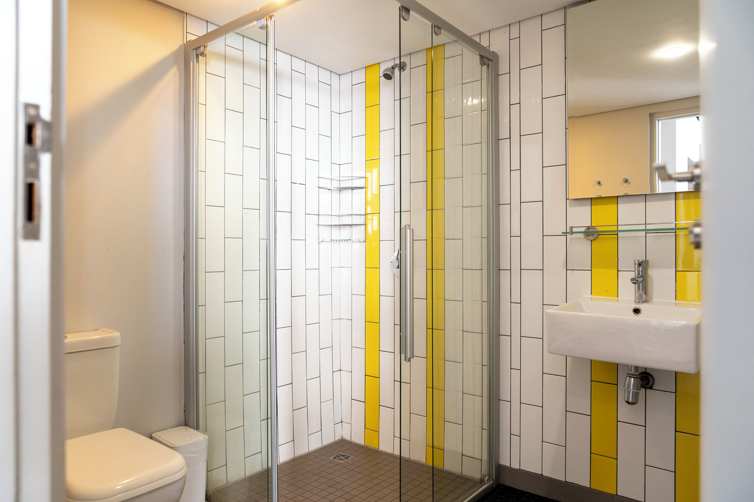Kylpyhuoneessa on lasiseinällä varustettu suihku, wc ja pesuallas, jonka yläpuolella on peili.