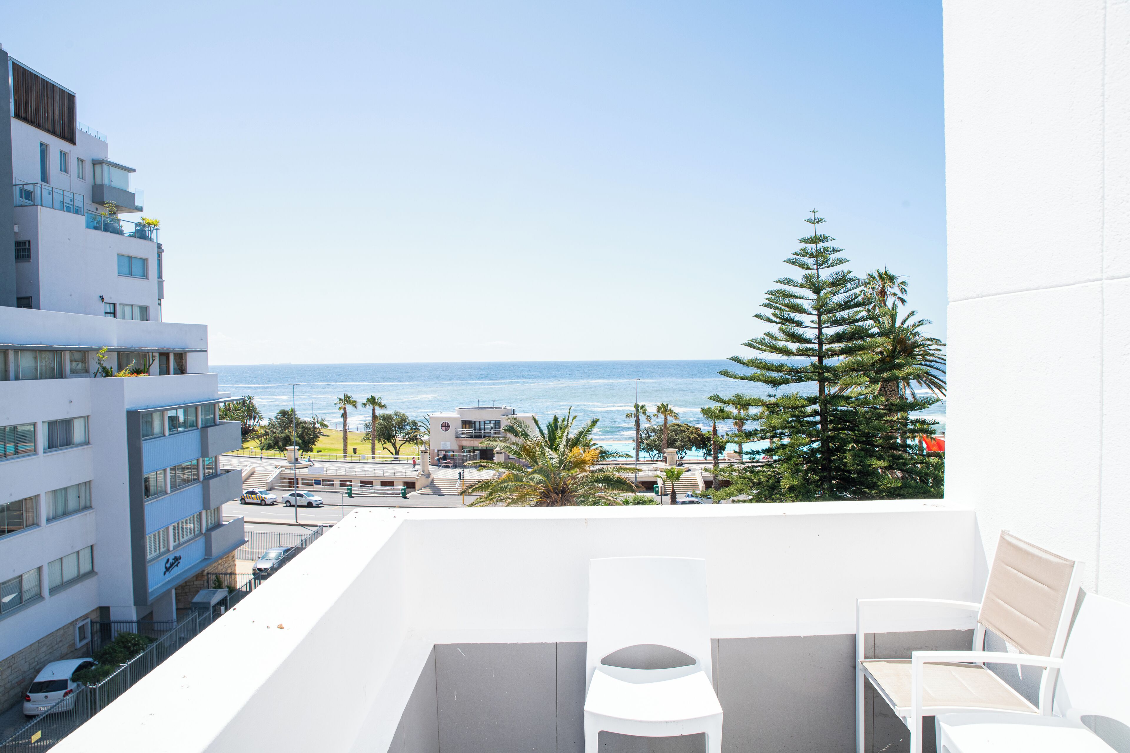 A balcony with white furniture, a view of the ocean, and buildings in the background.