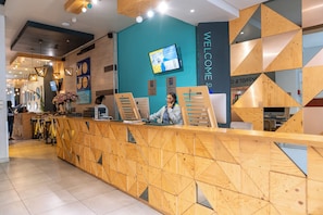 A reception desk with a geometric wood design, a TV screen, and a "WELCOME TO" sign.