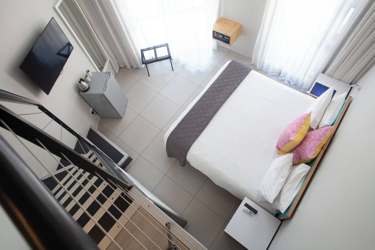 A hotel room with a bed, a TV, a small table, and a window with curtains.