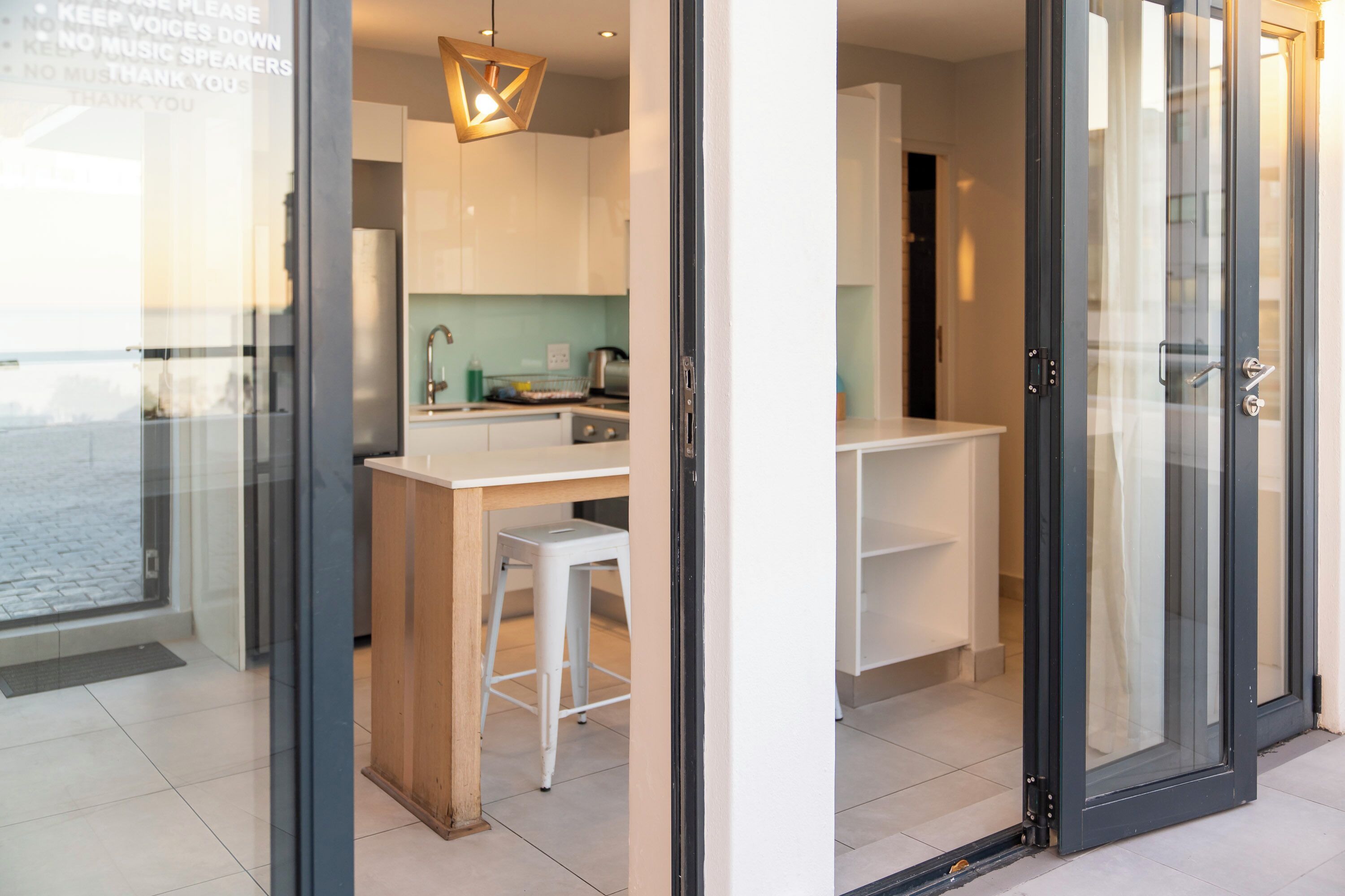 A modern kitchen with a bar area, a white stool, and a hanging light fixture.