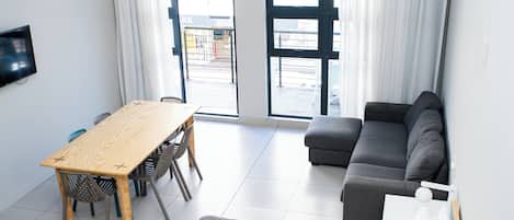 A modern living room with a sofa, a dining table with chairs, and a TV mounted on the wall.