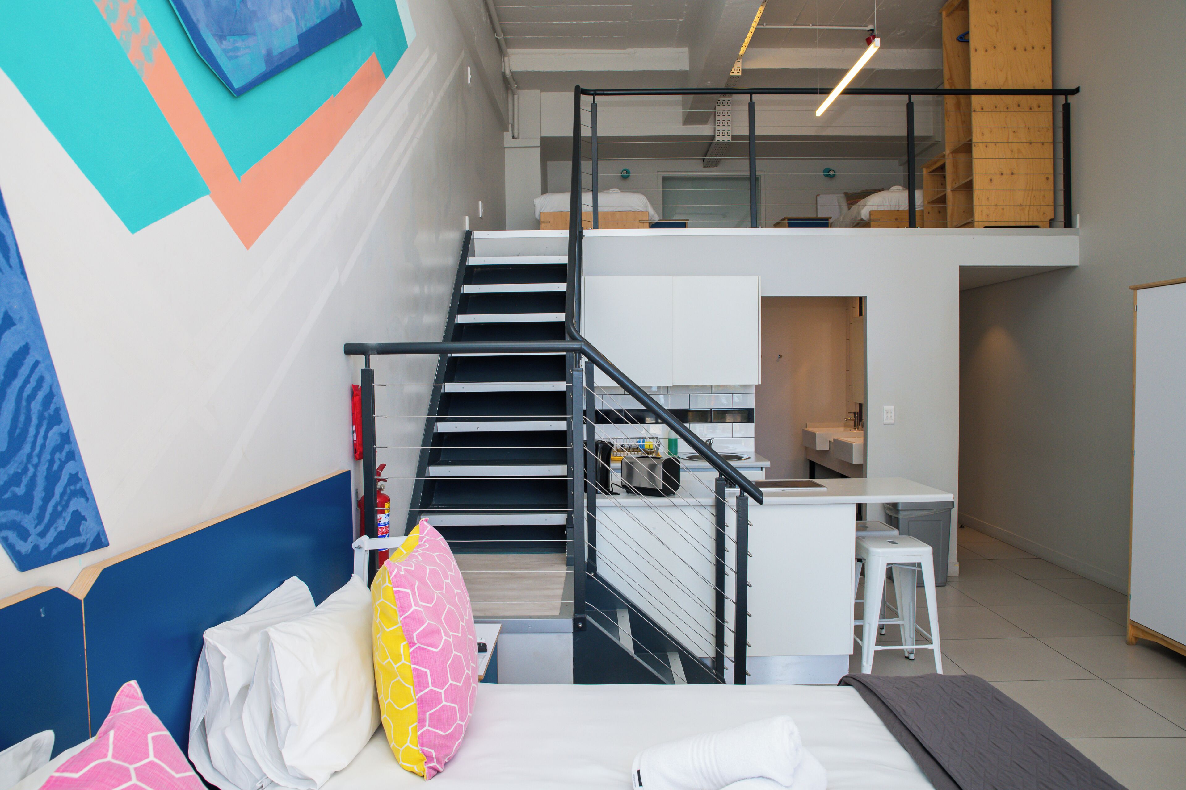 A modern hotel room with a bed, a desk, and a staircase.