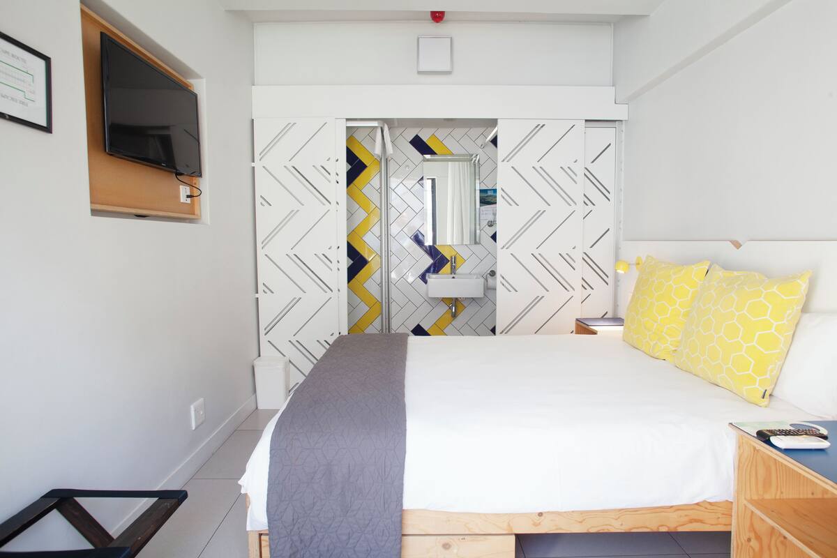 A modern bedroom with a bed, bedside table, and a TV mounted on the wall.