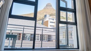 A room with large windows, an air conditioning unit, and a view of a mountain and buildings. - Mojo Hotel (Cape Town)