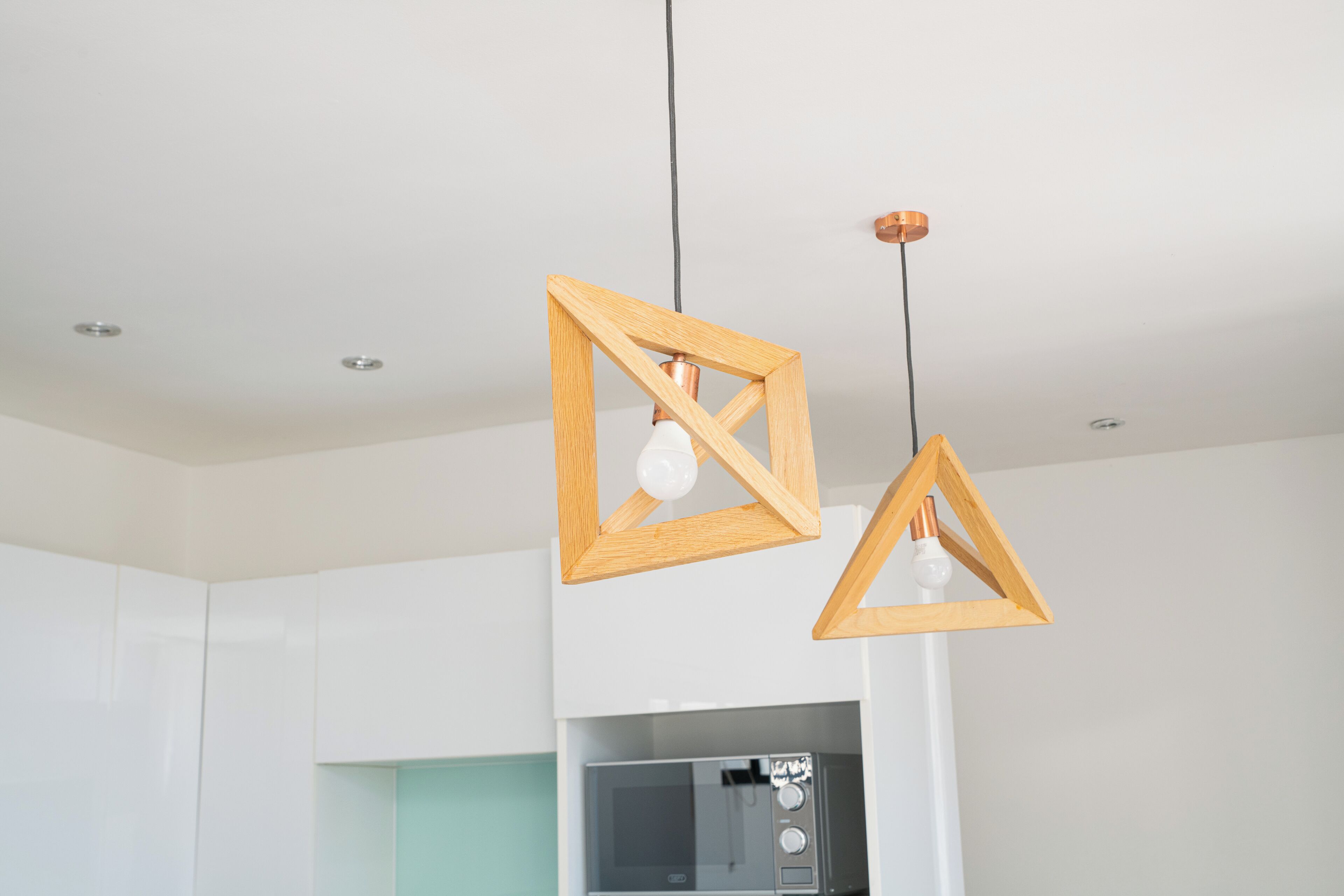 A kitchen with white cabinets, a microwave, and two wooden pendant lights with exposed bulbs.