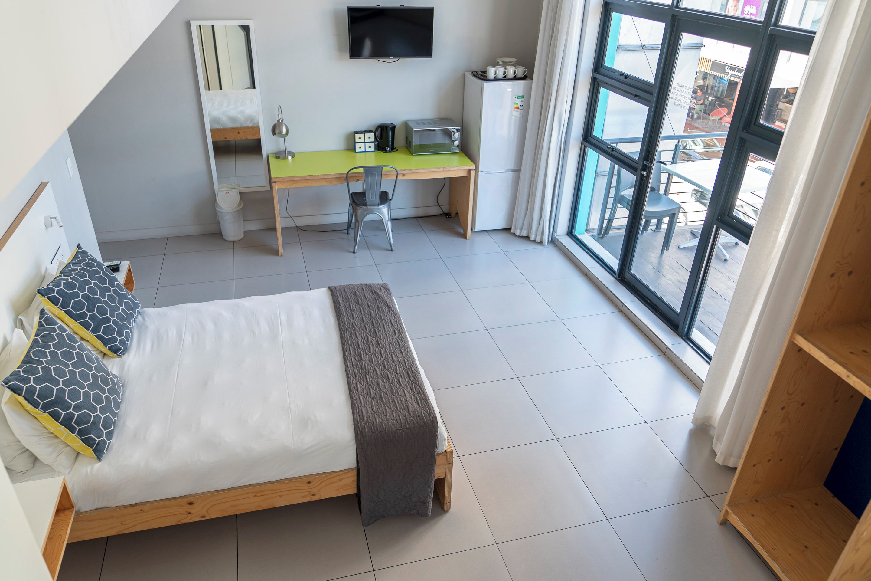 Un dormitorio con cama, escritorio, silla, televisor y ventana con vistas al exterior.