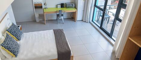 Un dormitorio con cama, escritorio, silla, televisor y ventana con vistas al exterior.