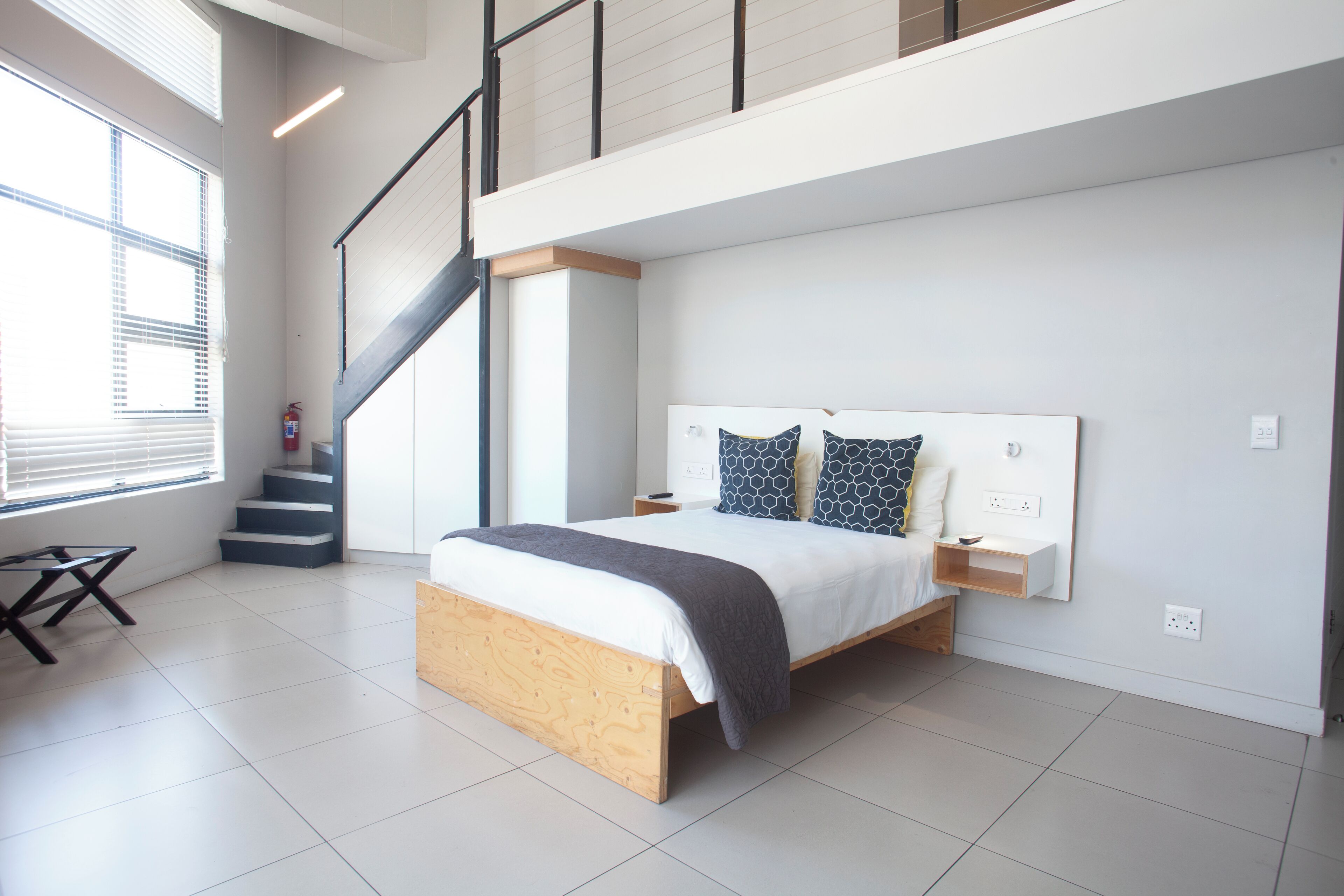 A modern bedroom with a wooden bed, a staircase, and a large window.
