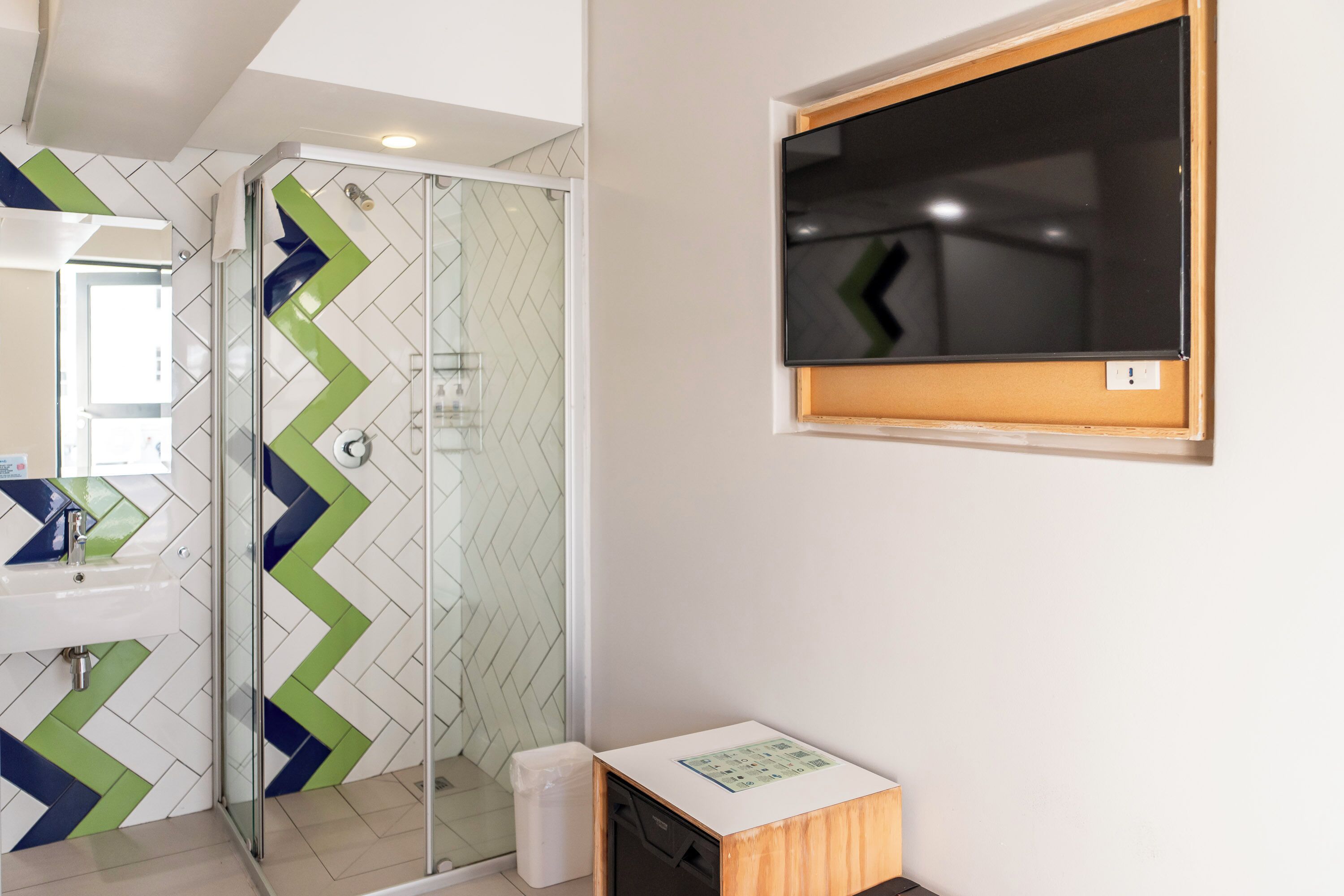 A modern bathroom with a glass shower enclosure, a sink, and a mounted television.