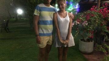 Two people standing in a garden at night with a Christmas tree and potted plants in the background.