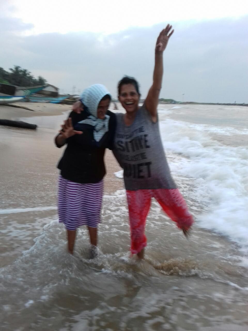 Two individuals standing in shallow water at a beach with waves.